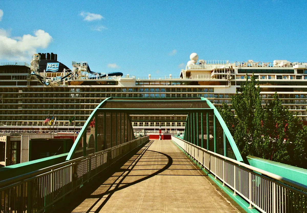 A green metal pedestrian bridge leading toward waterfront buildings in Seattle