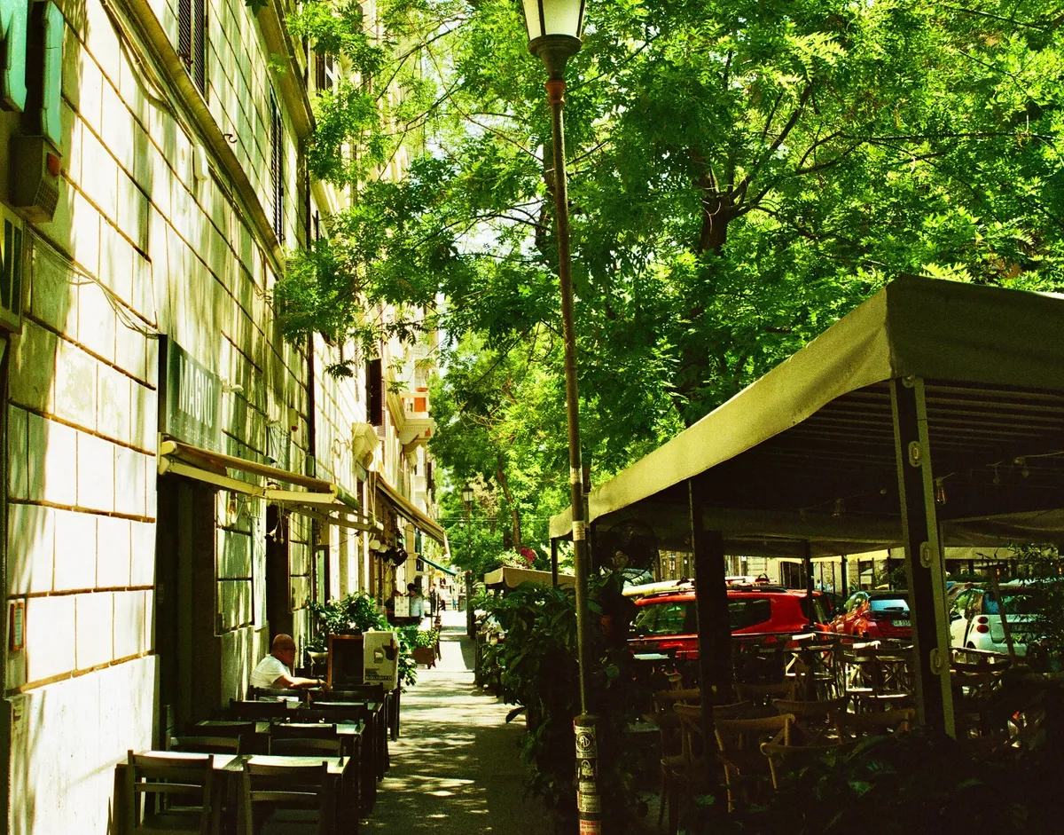 A leafy narrow street with outdoor café tables in Rome