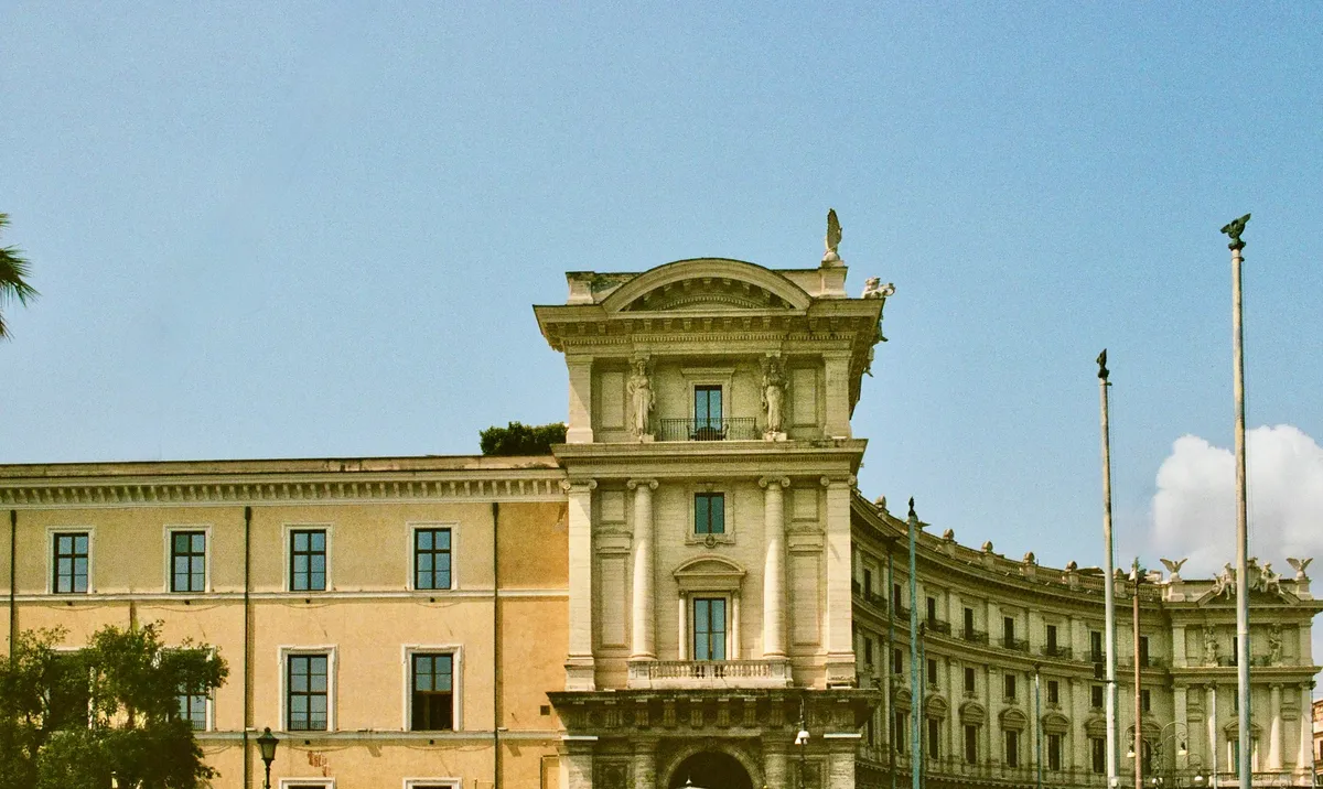 A pale yellow classical building beneath a clear blue sky in Rome