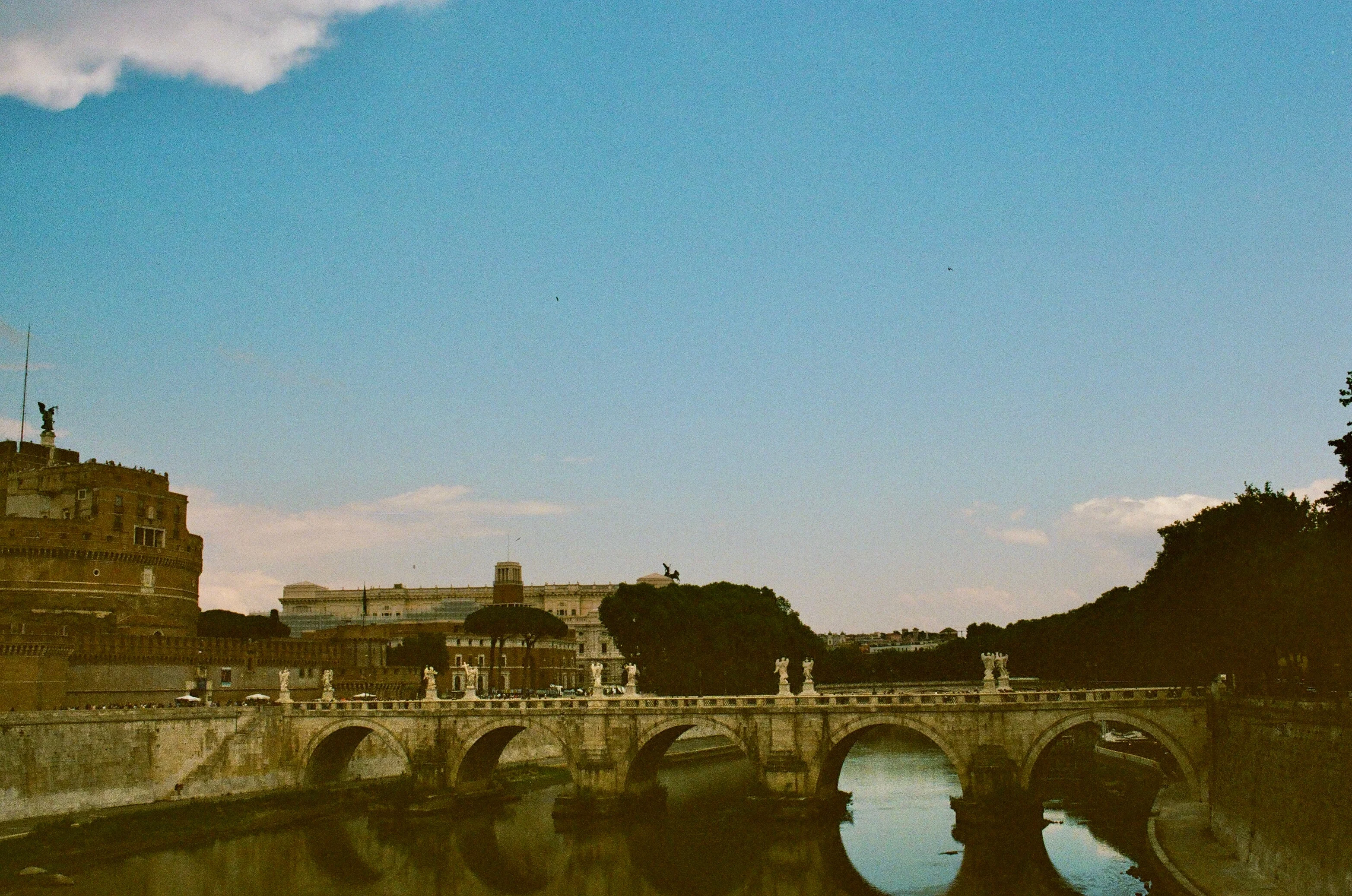 A stone bridge crossing the Tiber beneath a blue sky in Rome