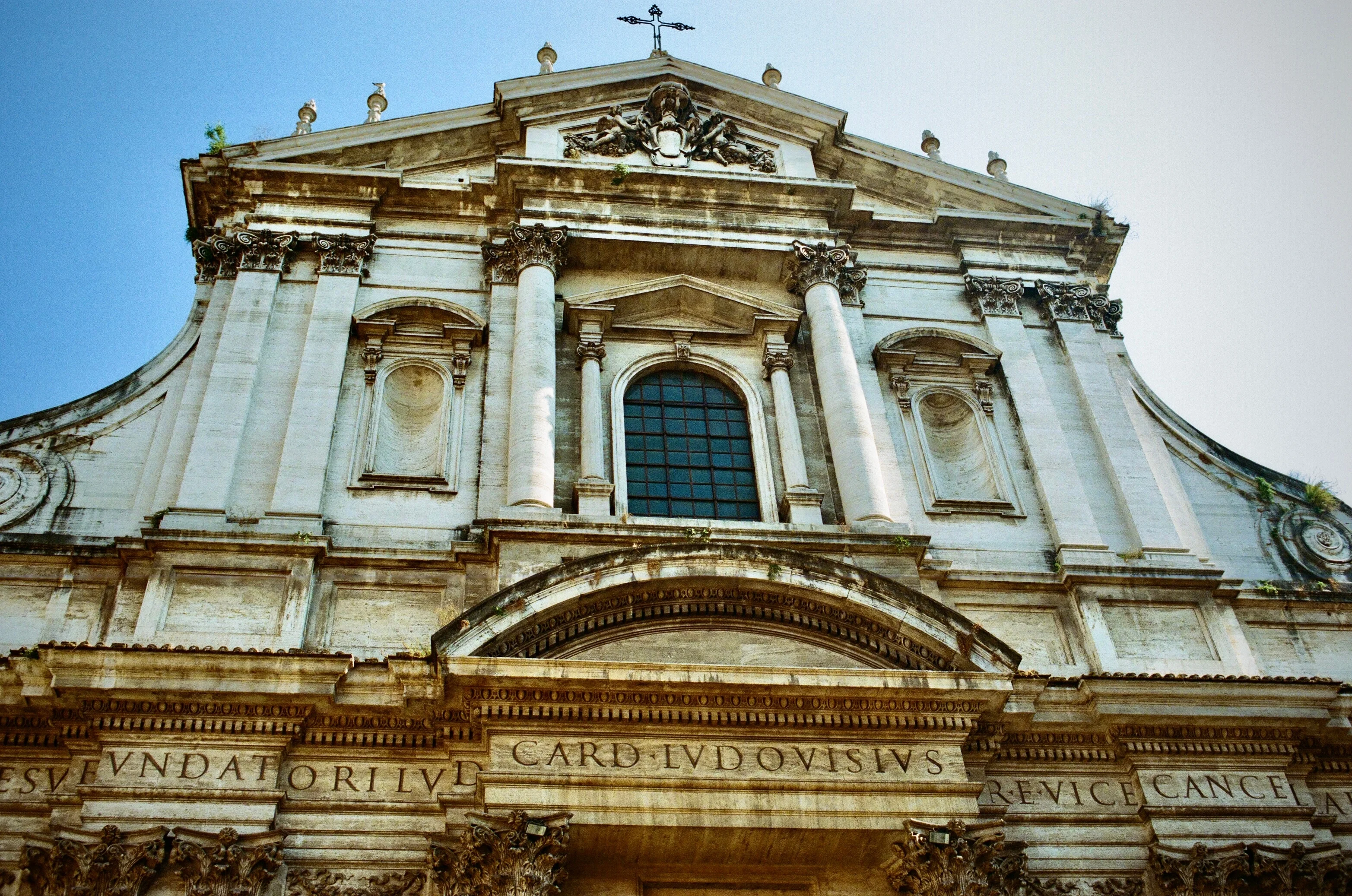 An ornate church facade viewed upward against a blue sky in Rome