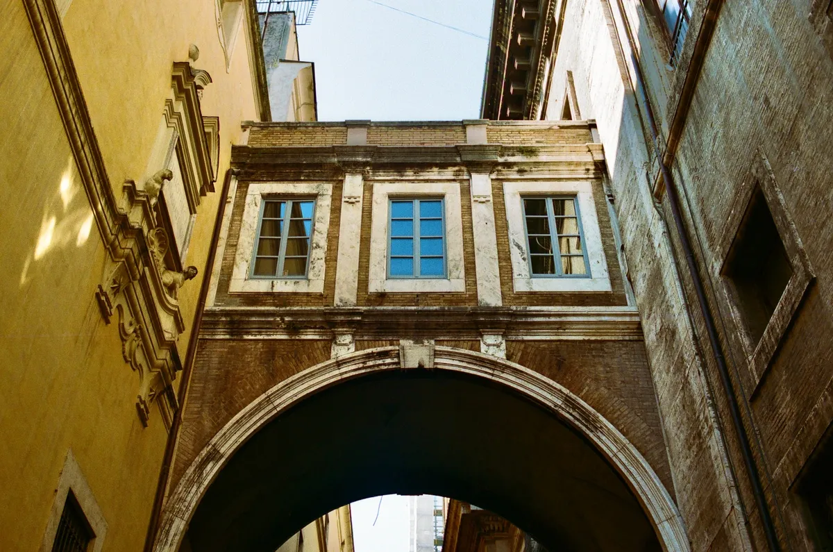 An enclosed passage bridging a narrow street between old buildings in Rome