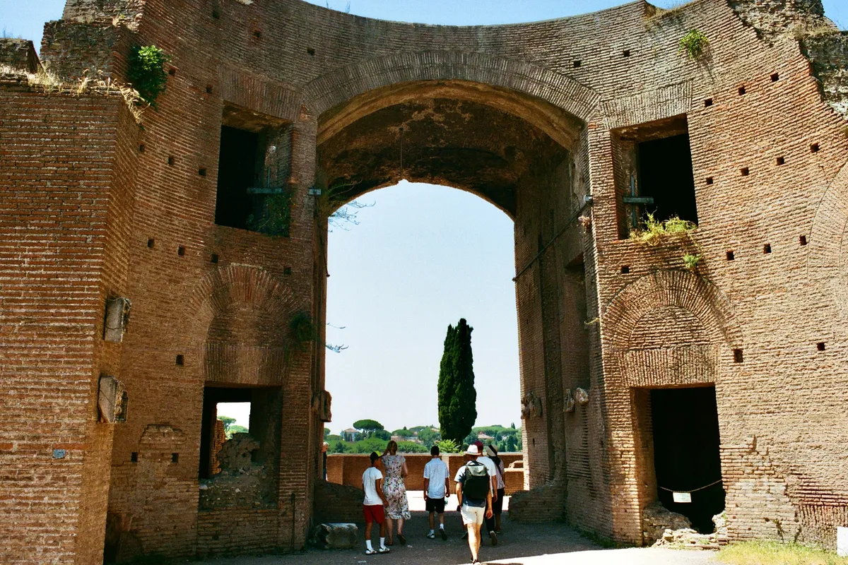Visitors walking through a monumental brick archway in Rome