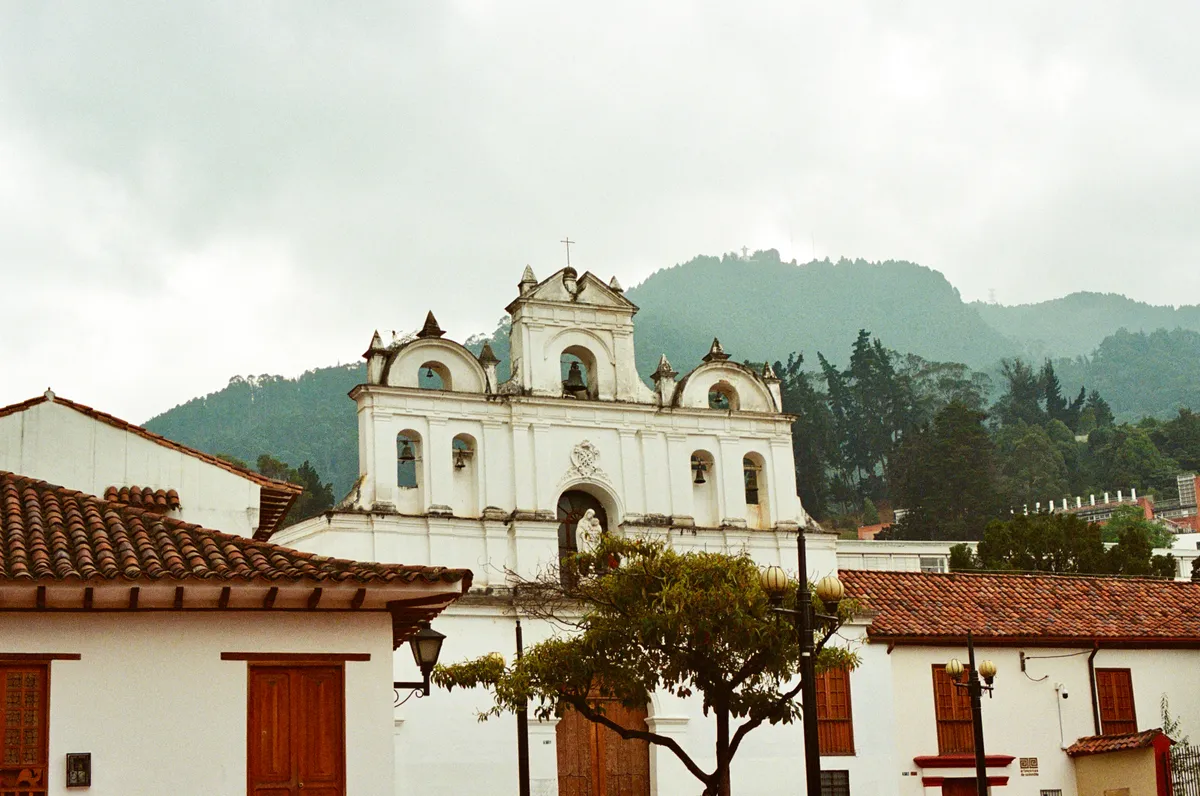 A white church rising above red tiled roofs with mountains behind it in Bogota