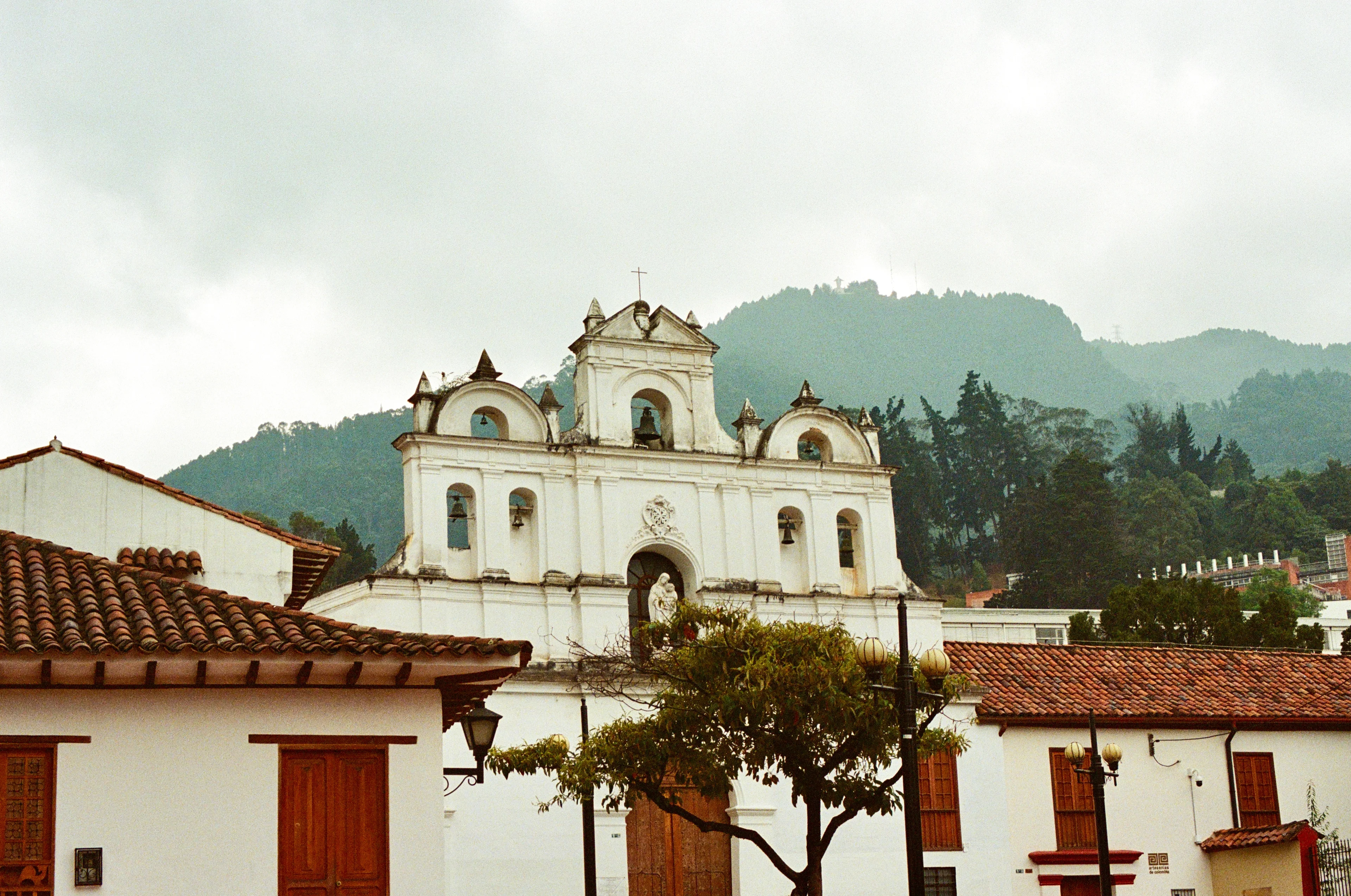 A white church rising above red tiled roofs with mountains behind it in Bogota