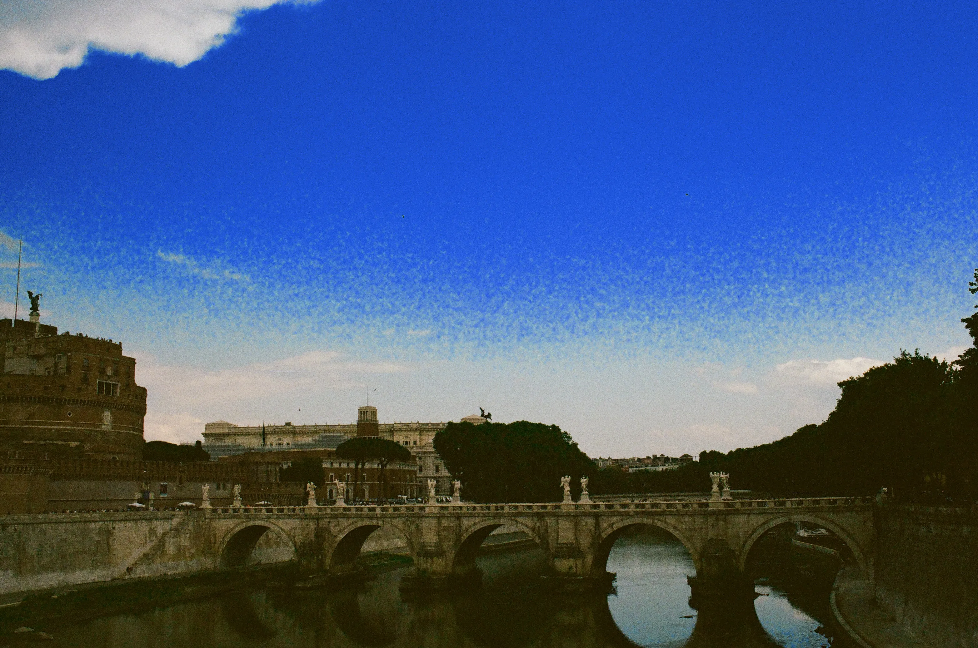 Elliot's film photograph of the Tiber and a stone bridge in Rome, graded with a deep blue sky.